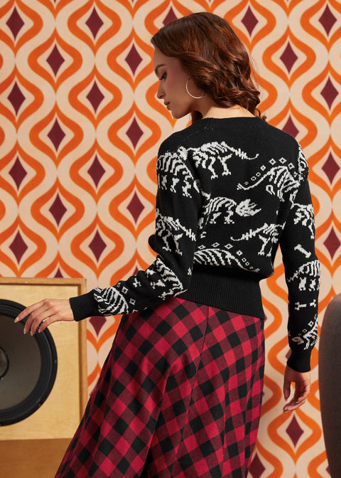 A woman shown from the back wearing a black knit sweater with white dinosaur skeleton patterns and a red-and-black plaid skirt, standing in front of a retro orange and cream patterned wall.