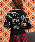 Woman wearing black cardigan with white dinosaur skeleton pattern and red-and-black plaid skirt, back view