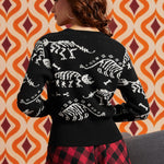 Woman wearing black cardigan with white dinosaur skeleton pattern and red-and-black plaid skirt, back view