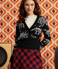 Woman wearing black cardigan with white dinosaur skeleton pattern over a white top and red-and-black plaid skirt, front view