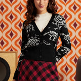 Woman wearing black cardigan with white dinosaur skeleton pattern over a white top and red-and-black plaid skirt, front view