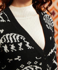 Close-up of black dinosaur skeleton cardigan showing deep V-neckline, black button front, ribbed trim, and white layering top