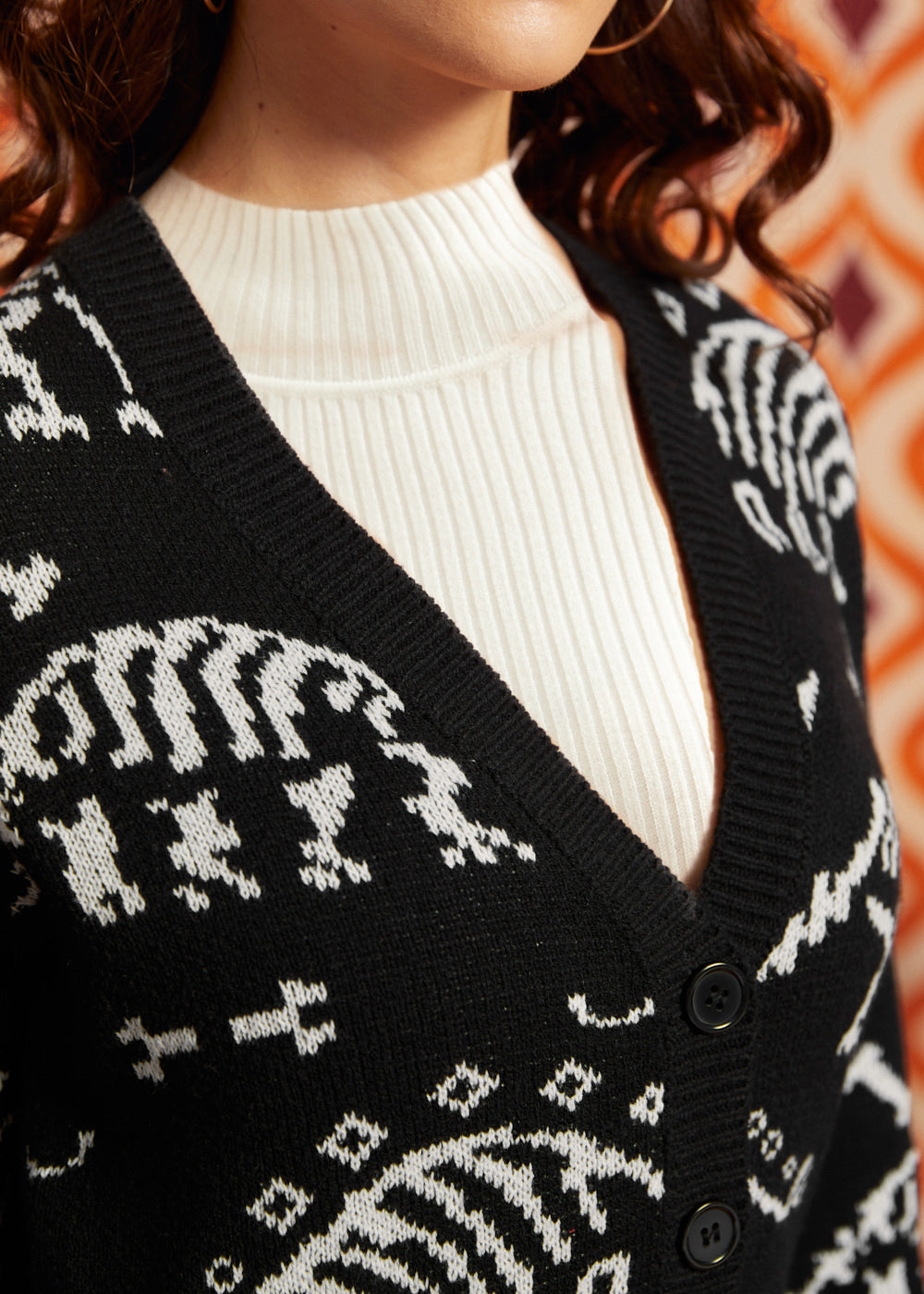 Close-up of black dinosaur skeleton cardigan showing deep V-neckline, black button front, ribbed trim, and white layering top