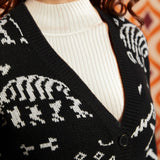 Close-up of black dinosaur skeleton cardigan showing deep V-neckline, black button front, ribbed trim, and white layering top