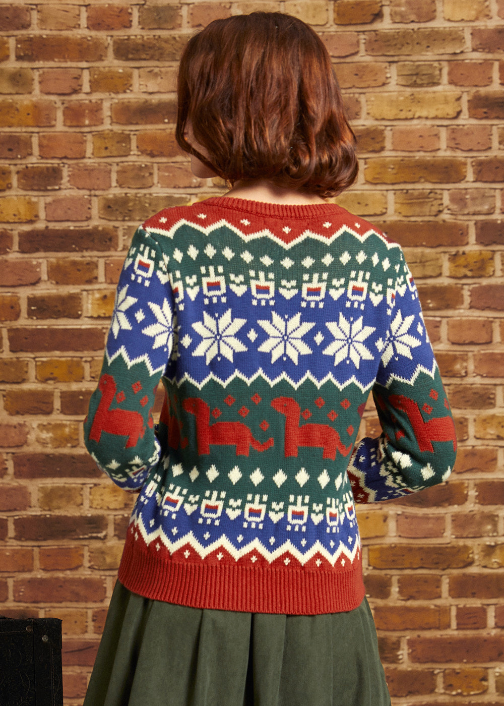 Back view of woman wearing colorful dinosaur Fair Isle sweater with repeating geometric and prehistoric motifs