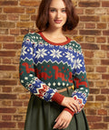 A woman wearing a festive Christmas sweater with a blue, green, and red holiday pattern, standing against a rustic brick wall.