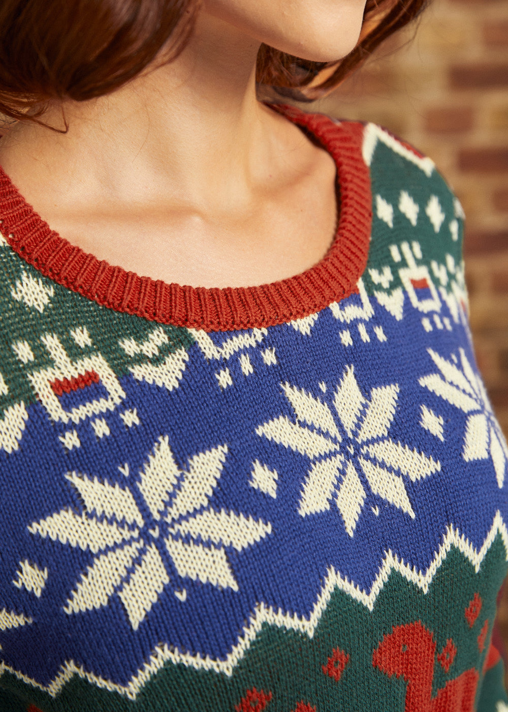 Close-up of 100% cotton dinosaur Fair Isle sweater showing cobalt blue knit, cream motifs, and rust ribbed crew neckline
