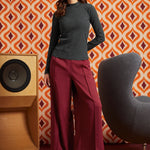 Woman wearing the striped mock neck top tucked into high-waisted burgundy trousers