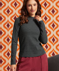 Woman wearing a black and gray striped mock neck long sleeve top with burgundy trousers, front view