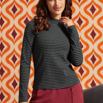 Woman wearing a black and gray striped mock neck long sleeve top with burgundy trousers, front view