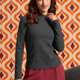 Woman wearing a black and gray striped mock neck long sleeve top with burgundy trousers, front view