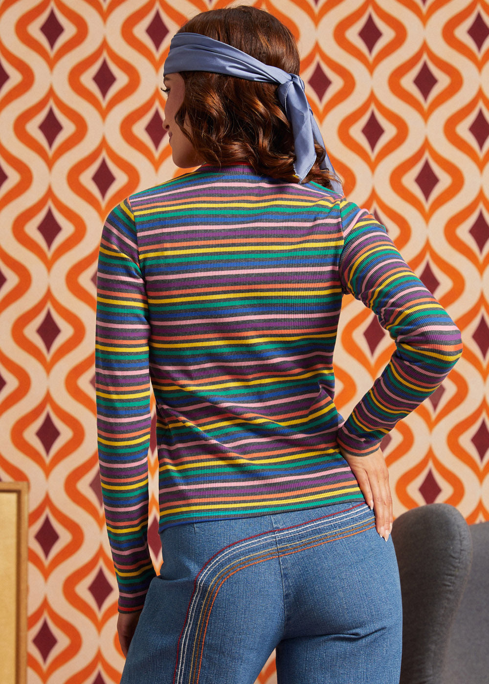 Woman wearing a rainbow striped mock neck long sleeve top with blue jeans, back view