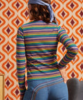 Woman wearing a rainbow striped mock neck long sleeve top with blue jeans, back view