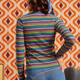Woman wearing a rainbow striped mock neck long sleeve top with blue jeans, back view
