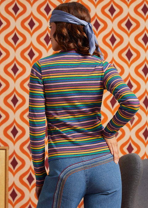 Woman wearing a rainbow striped mock neck long sleeve top with blue jeans, back view