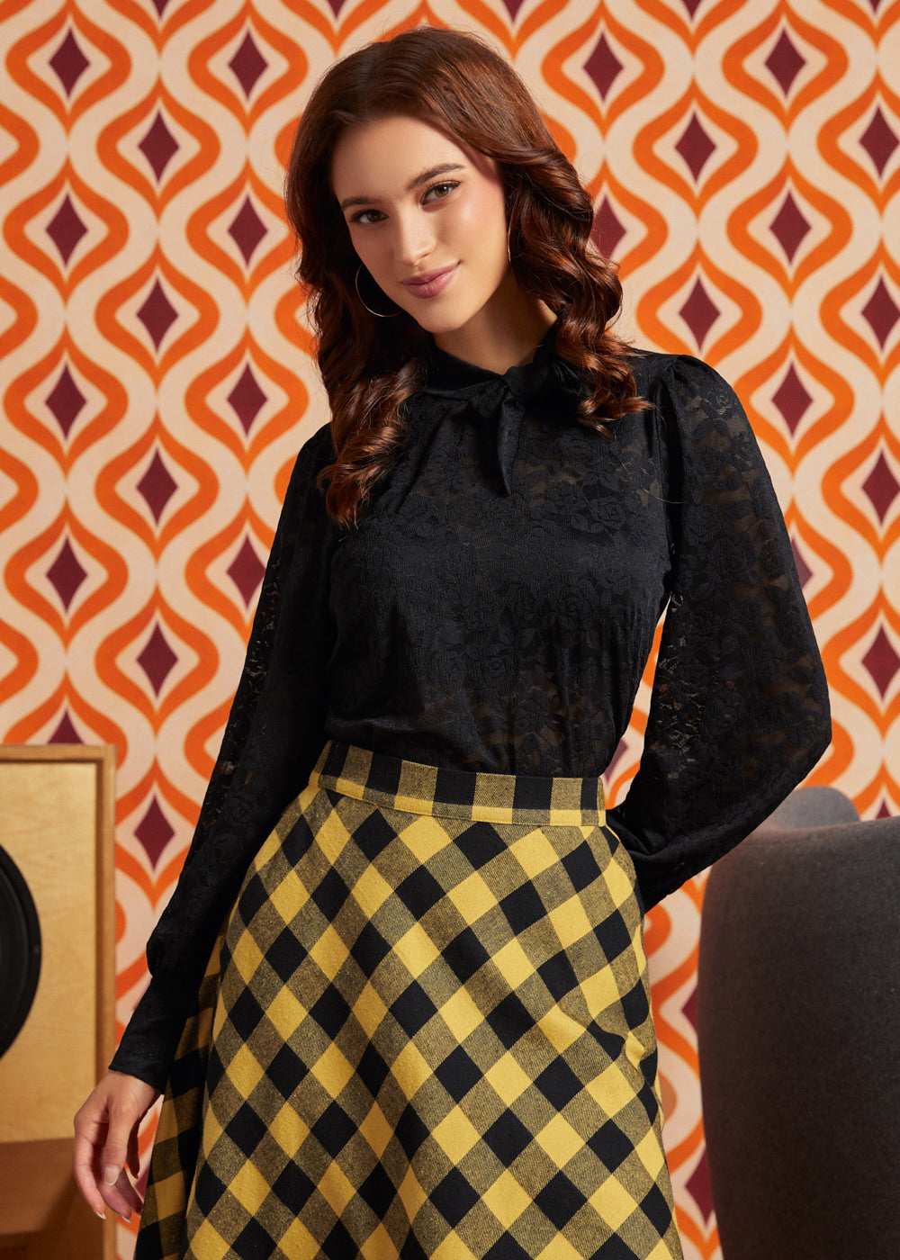 Woman wearing black floral lace puff sleeve top from the back with a yellow and black check midi skirt.