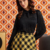 Woman wearing black floral lace puff sleeve top from the back with a yellow and black check midi skirt.
