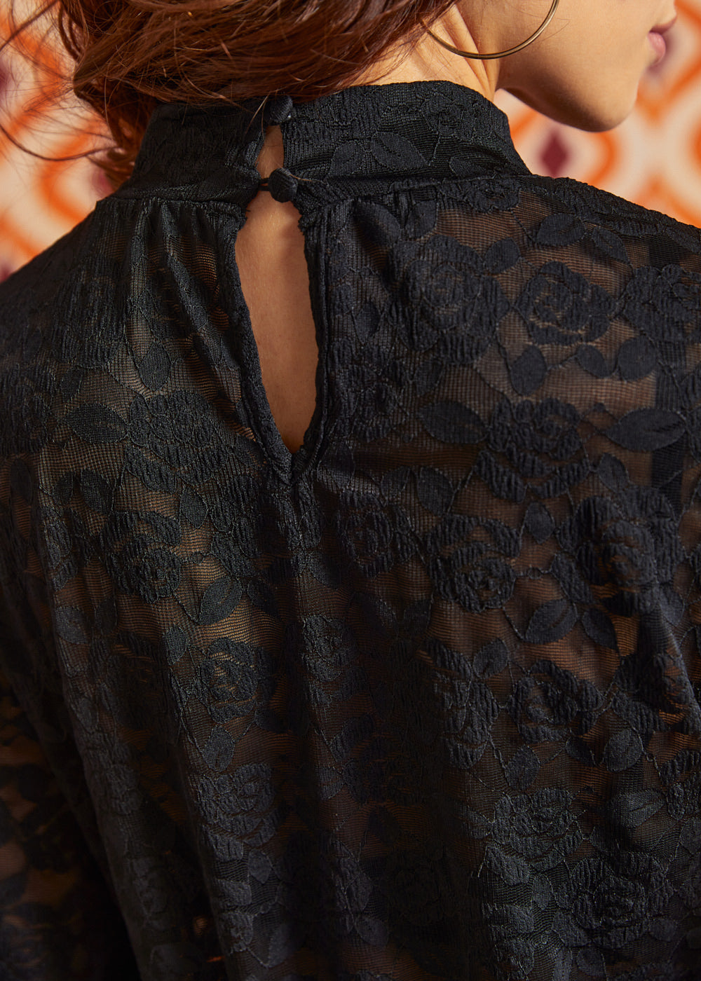 Close-up back view of black floral lace top showing the high neckline, button-and-loop closure, and keyhole opening.