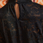 Close-up back view of black floral lace top showing the high neckline, button-and-loop closure, and keyhole opening.