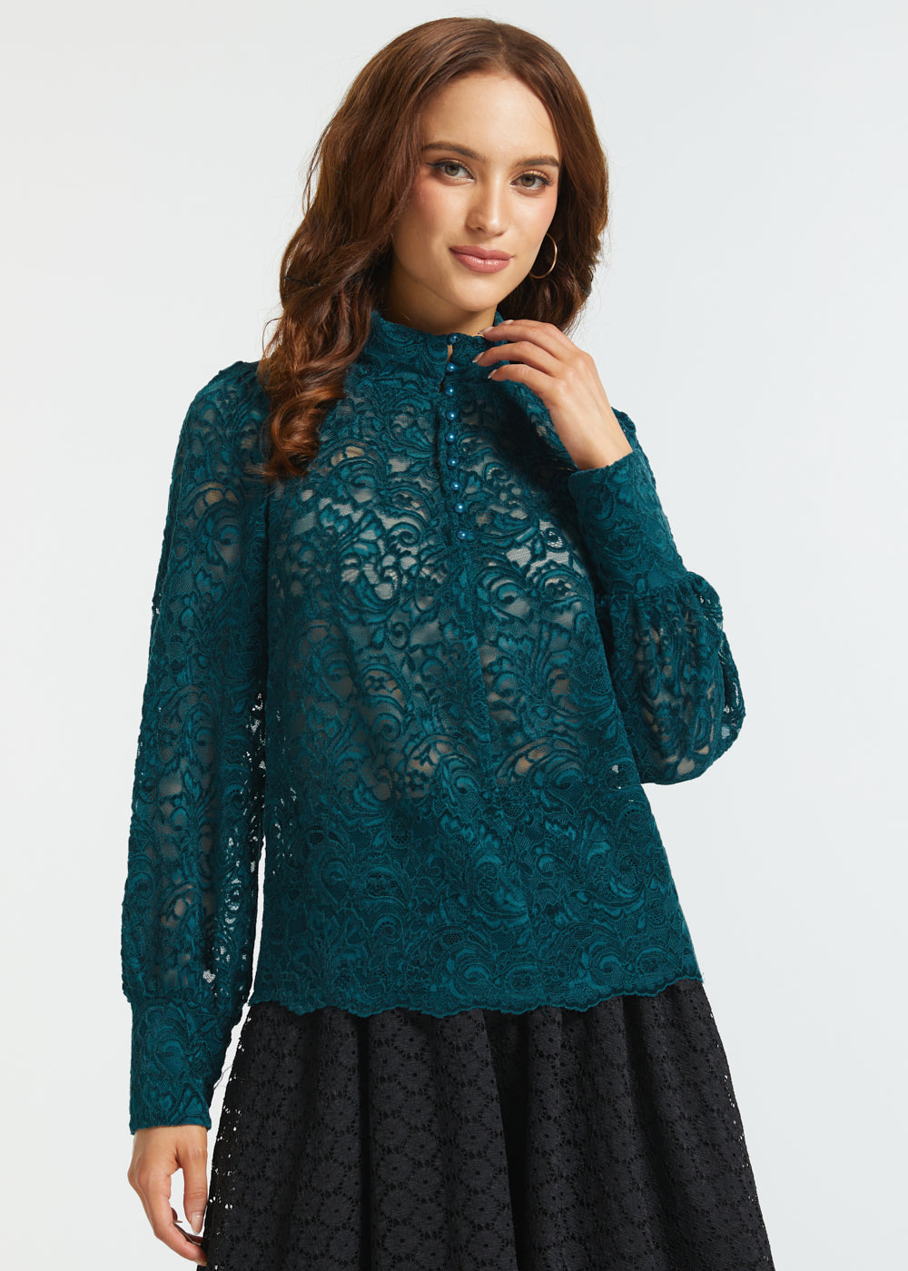 Woman wearing a teal Victorian-inspired lace blouse with high neckline, pearl-like buttons, sheer long sleeves, and scalloped hem against a white background.
