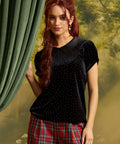 Model wearing a black velvet short sleeve top with tiny metallic stud embellishments, contrasting Peter Pan collar, and puff sleeves, paired with red plaid trousers.