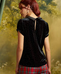 Rear view of a black velvet blouse with scattered metallic nailhead studs, short puff sleeves, contrasting collar, and keyhole back opening with button closure.