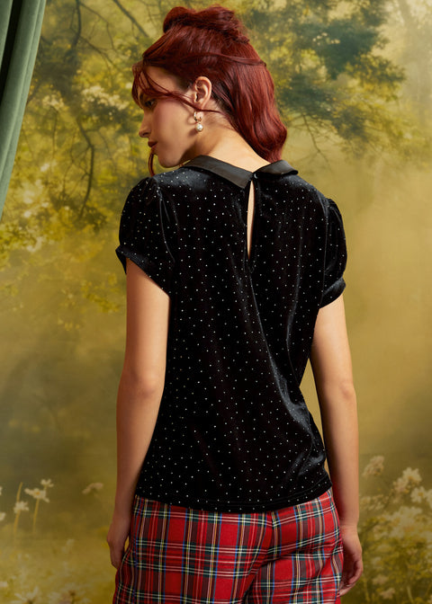 Rear view of a black velvet blouse with scattered metallic nailhead studs, short puff sleeves, contrasting collar, and keyhole back opening with button closure.