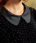 Close-up of a black velvet top showing the smooth Peter Pan collar, and tiny heat-set metallic nailhead studs across the fabric.