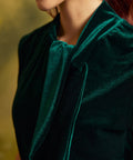 Close-up of the emerald green velvet top showing the soft, lustrous fabric and draped statement neck tie.
