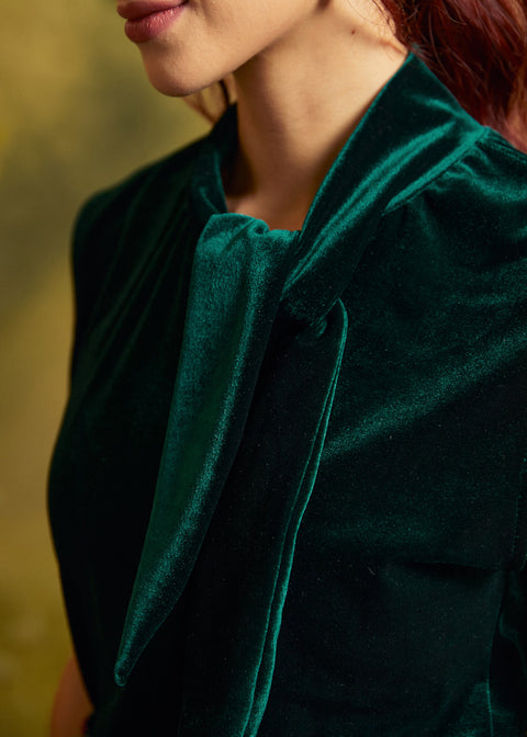 Close-up of the emerald green velvet top showing the soft, lustrous fabric and draped statement neck tie.