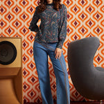 Woman wearing a blue paisley mock neck top with long bishop sleeves and wide-leg jeans, front full-length view