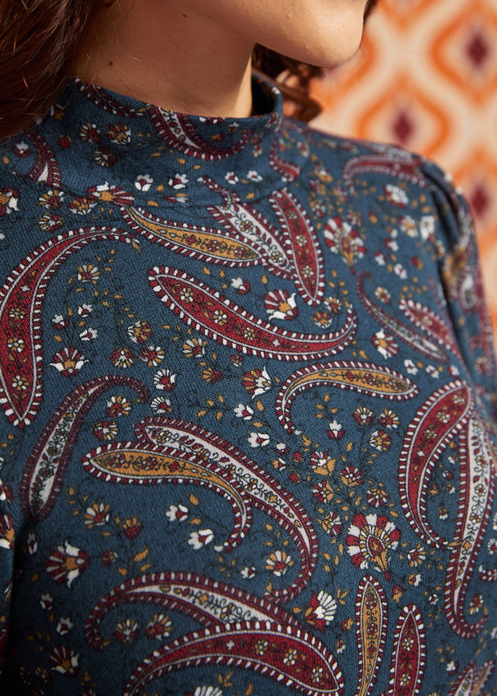 Close-up of blue, burgundy, mustard, and cream paisley print and mock neckline