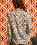 Woman wearing cream bird print blouse with brown skirt, back view showing long sleeves and shirttail hem