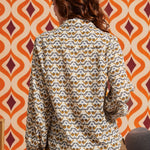 Woman wearing cream bird print blouse with brown skirt, back view showing long sleeves and shirttail hem