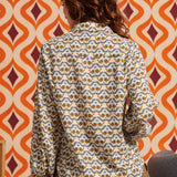 Woman wearing cream bird print blouse with brown skirt, back view showing long sleeves and shirttail hem