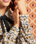 Close-up of long gathered sleeves and buttoned cuffs on cream bird print blouse with black necktie