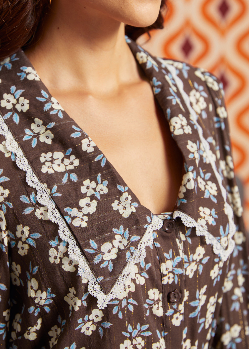 Close-up of brown floral blouse with blue and cream flowers, metallic pinstripes, oversized pointed collar, and delicate white lace trim.