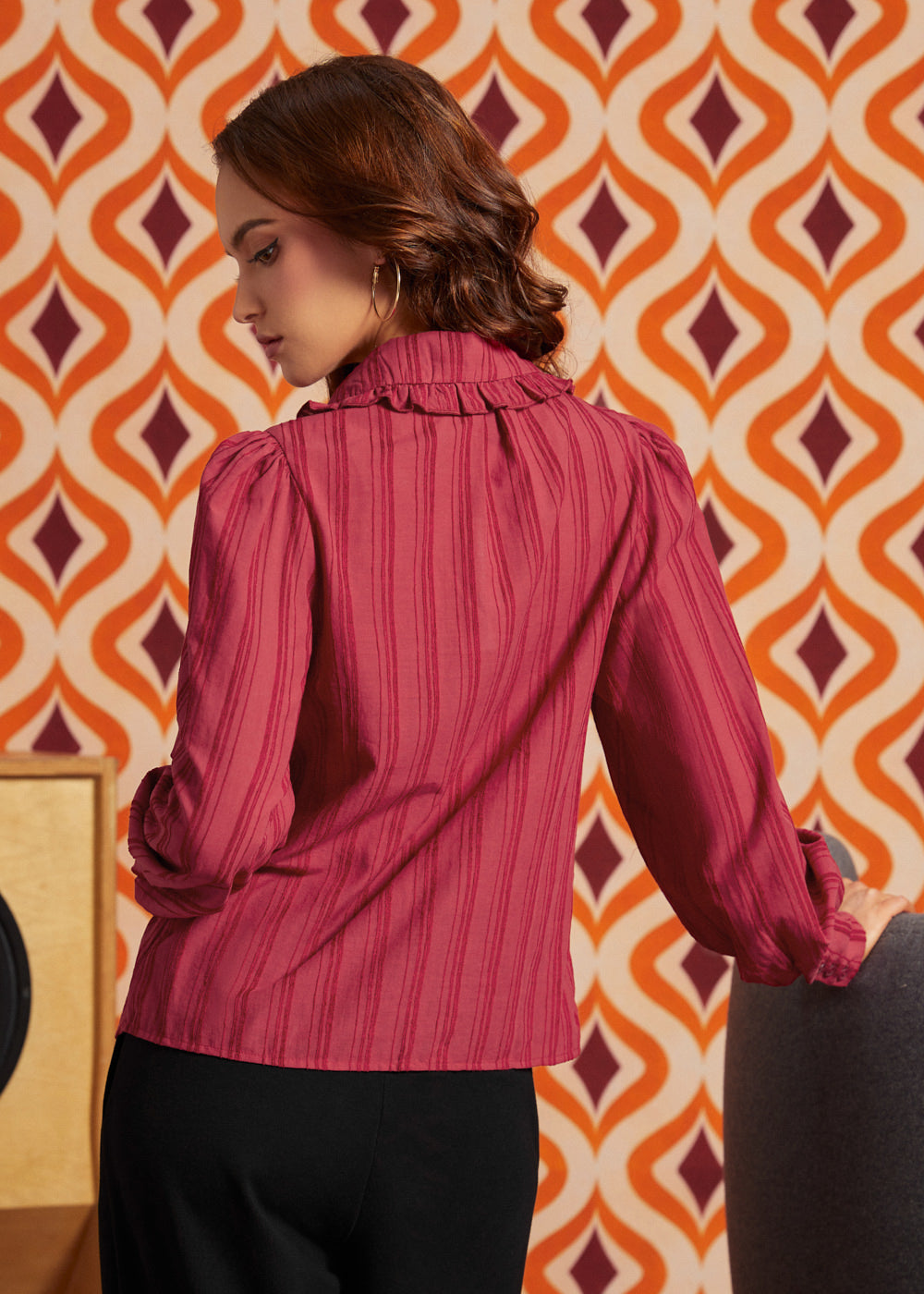 Woman wearing the raspberry long sleeve blouse from the back, showing gathered shoulders, ruffled collar, and tonal stripe texture.