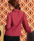 Woman wearing the raspberry long sleeve blouse from the back, showing gathered shoulders, ruffled collar, and tonal stripe texture.