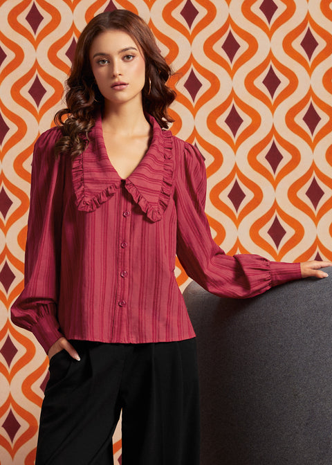 A woman wearing a long-sleeve ruffled blouse in a deep magenta pink with vertical stripes, paired with black pants
