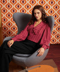 A woman sits in a gray modern egg chair, wearing a dark pink ruffled blouse and black trousers from ModCloth