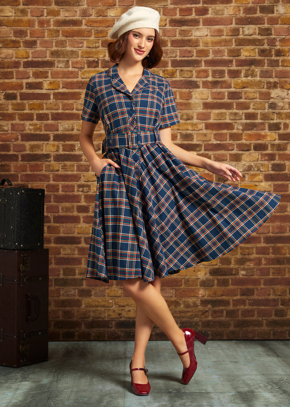 Woman wearing navy plaid cotton shirt dress with matching belt and side pockets, holding out the full skirt