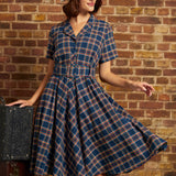 Woman wearing a navy plaid cotton fit-and-flare midi dress with short sleeves, button front, and matching buckle belt