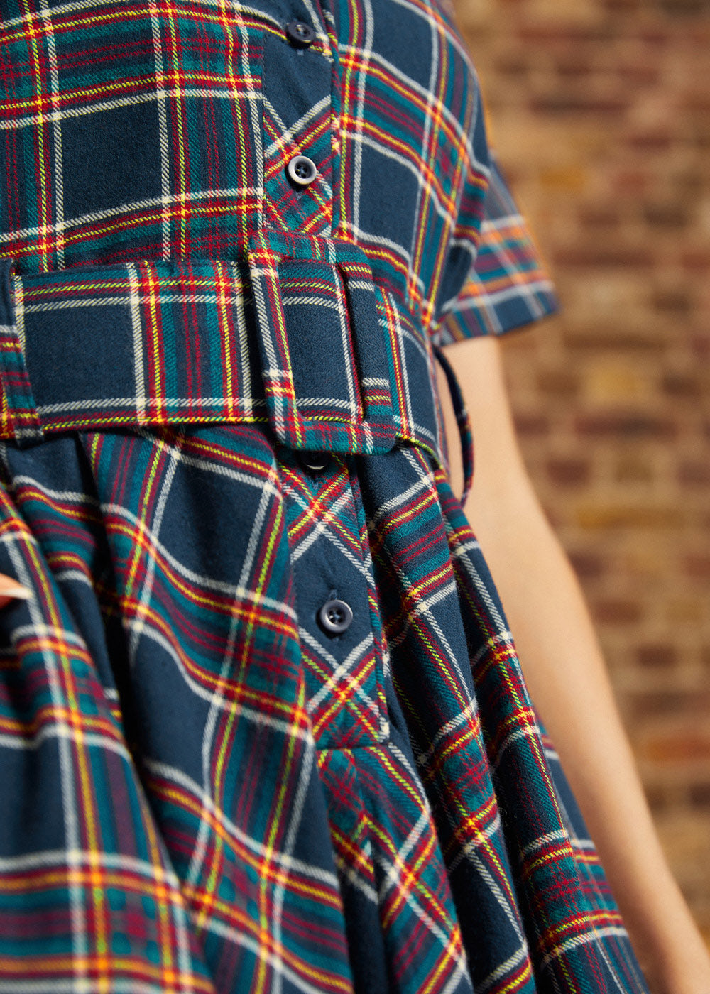 Close-up of plaid shirt dress showing functional button-front bodice, notched collar, and matching belt