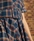 Close-up of plaid shirt dress showing functional button-front bodice, notched collar, and matching belt