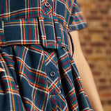 Close-up of plaid shirt dress showing functional button-front bodice, notched collar, and matching belt