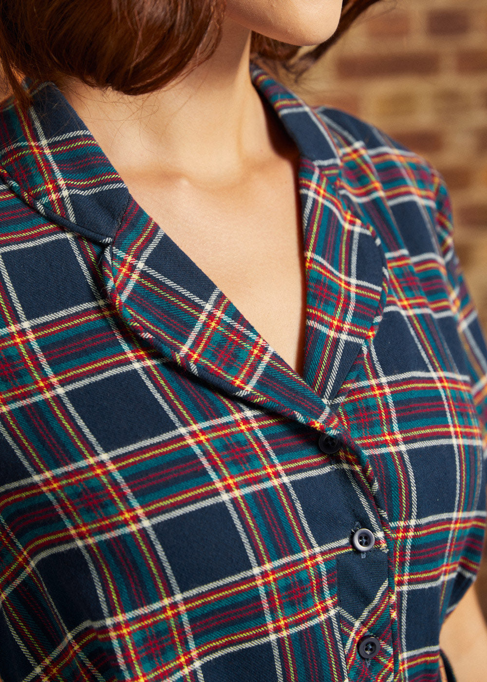Close-up of plaid shirt dress showing functional button-front bodice, notched collar, and matching belt