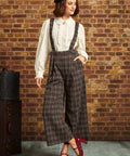 Woman wearing brown plaid wide-leg cropped suspender pants with an ivory ruffled blouse and red Mary Jane heels
