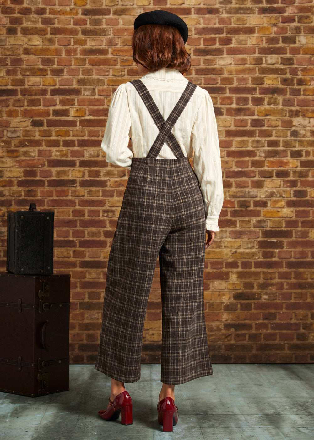 Back view of woman wearing brown plaid cropped pants with suspender straps crossed at the back