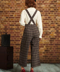 Back view of woman wearing brown plaid cropped pants with suspender straps crossed at the back